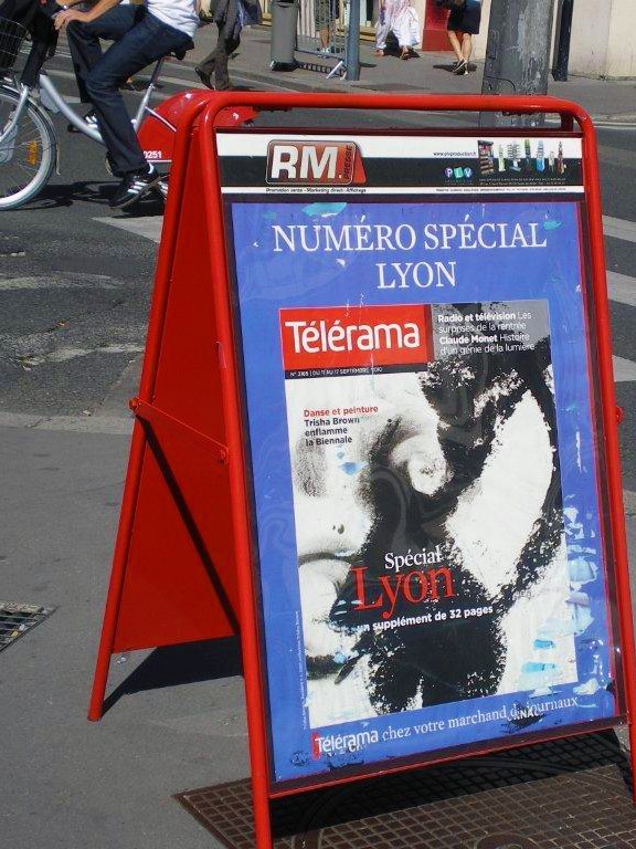 Chevalet d’affichage Martinez Presse sur un trottoir, passants et cyclistes autour